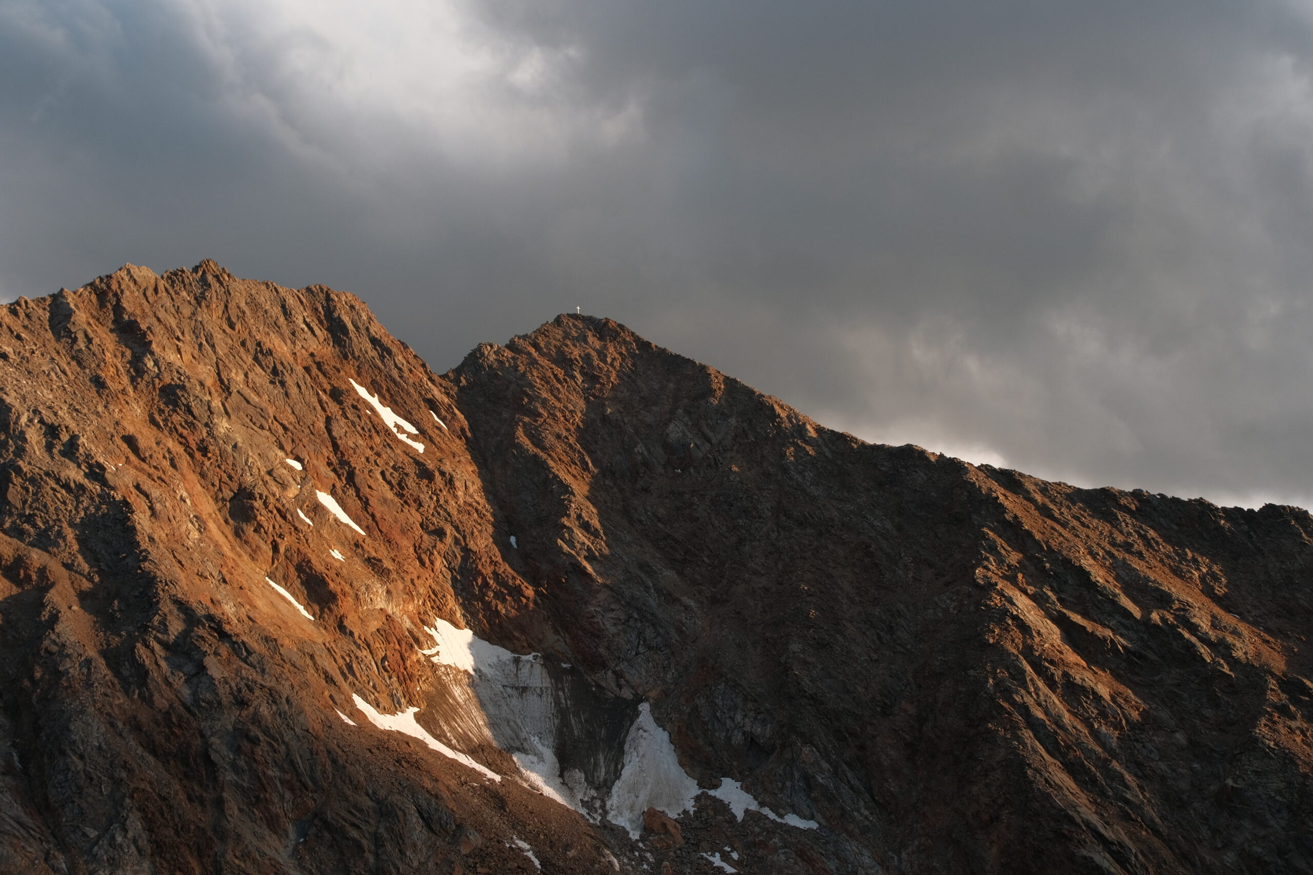 Felsiger Gipfel des Scheiblehnkogels im warmen Abendlicht unter dunklen Wolken – fotografiert von Bergkompass Bergwanderführer Pascal Schirmer